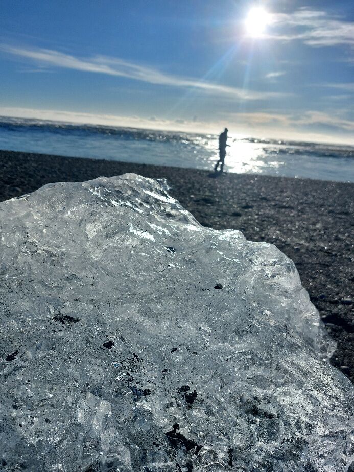 A huge ice cube at a black, volcanic beach, shining like a diamond in the sun